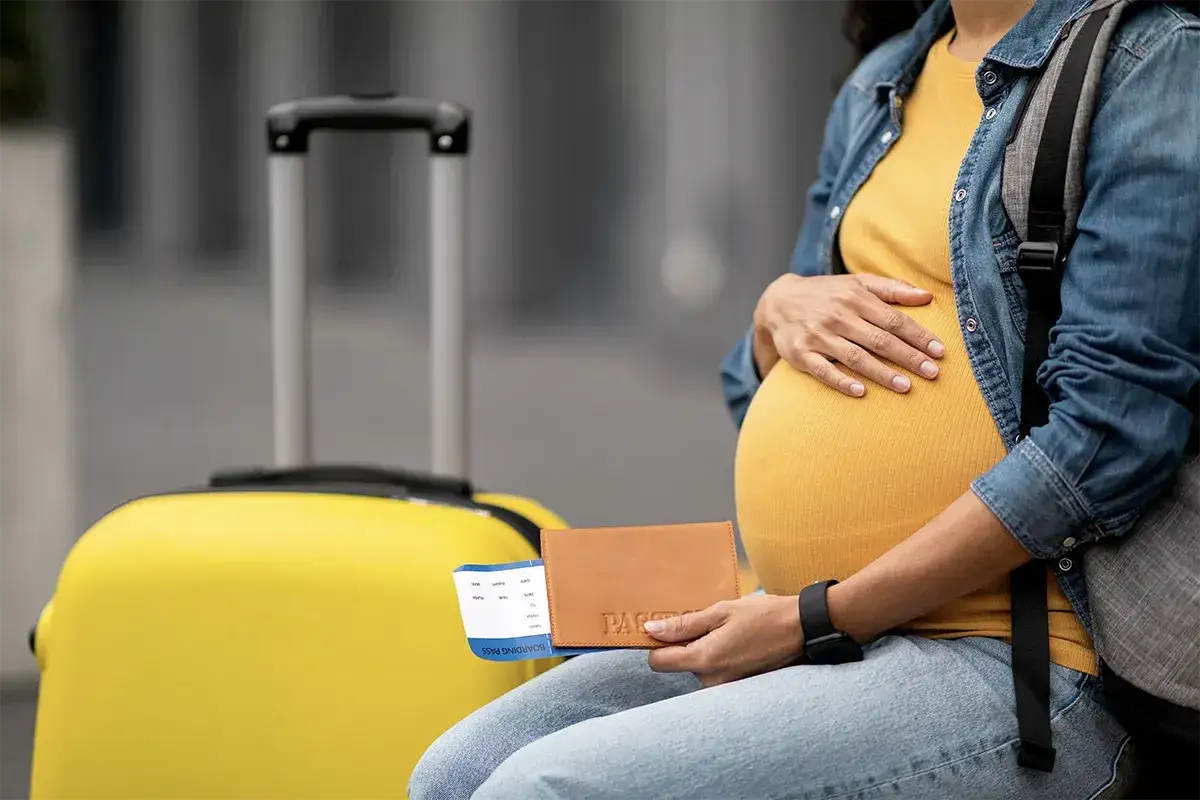 Donna incinta con valigia gialla, passaporto e biglietto aereo. Un viaggio in aereo in gravidanza è possibile.