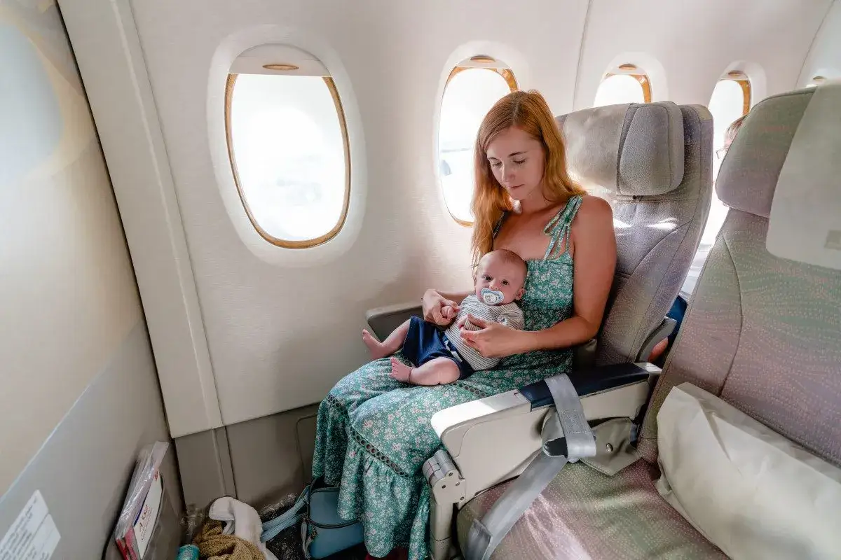 Mamma con neonati in aereo, seduta vicino al finestrino, accarezza il suo bimbo con ciuccio.