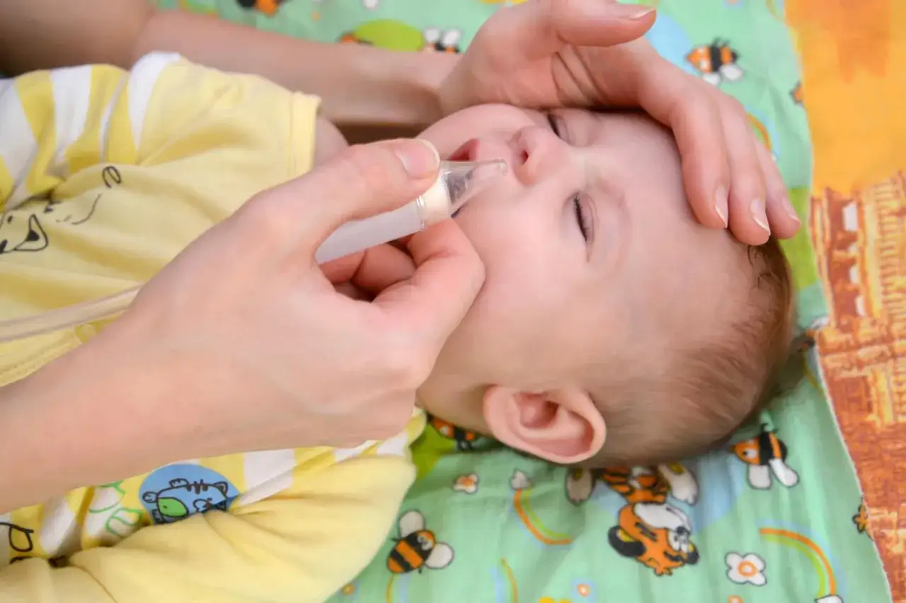 Mano che usa un aspiratore nasale per liberare il naso chiuso di un neonato, senza muco visibile.
