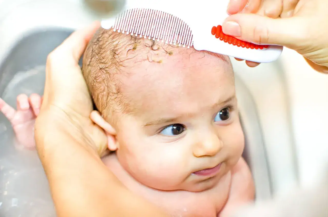Mani delicate rimuovono la crosta lattea dal cuoio capelluto di un neonato con un pettinino apposito.