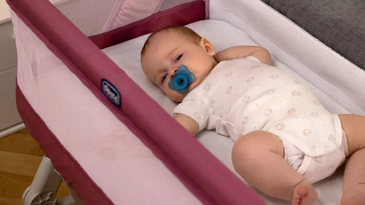 Dolce neonato dorme sul fianco in una culla, con un ciuccio blu in bocca.