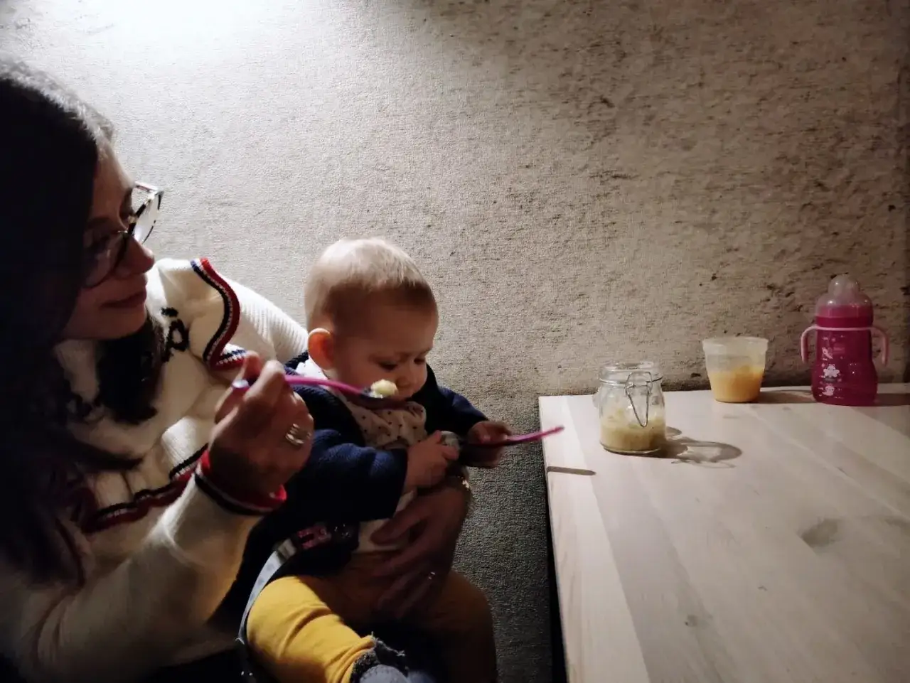 Mamma d&agrave; la pappa al suo bimbo fuori casa, con un vasetto di omogeneizzato e biberon pronti.