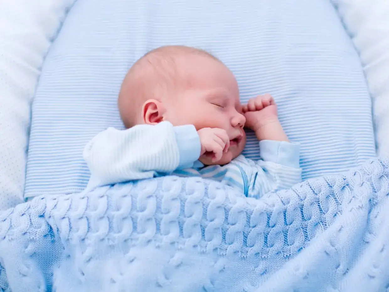 Un neonato dorme sereno, avvolto in una coperta azzurra. Sembra che i neonati possano mangiare mentre dormono, un piccolo miracolo della natura.