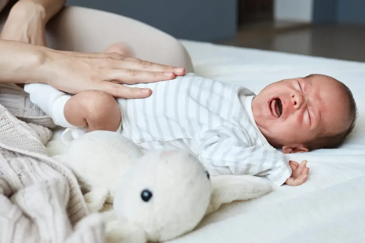 Un neonato piange disperato, con la mano di un adulto che gli accarezza la pancia. Come capire se il neonato ha le coliche.