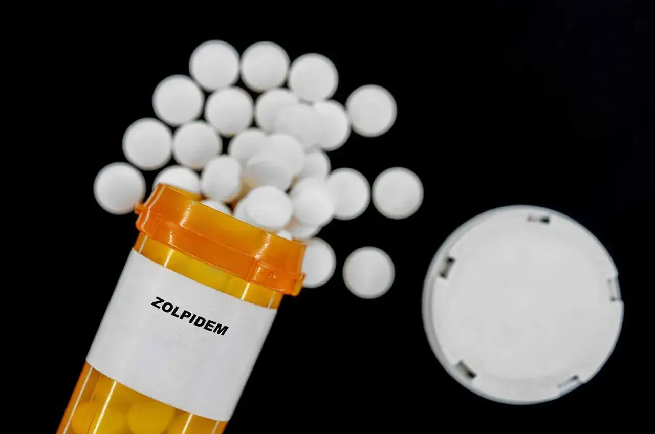 Pillole di Zolpidem 10 mg fuori da un flacone arancione su sfondo nero.