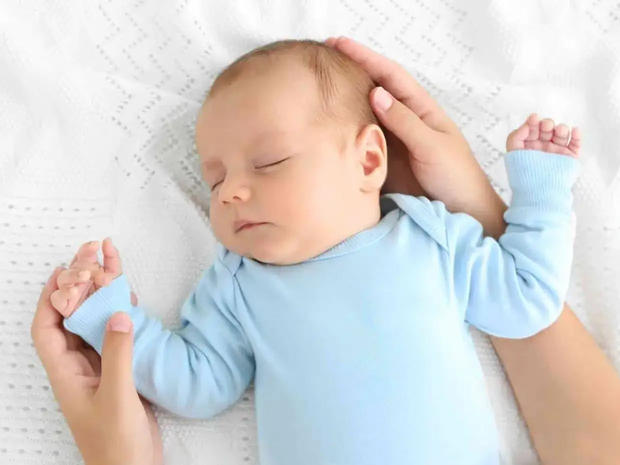 Un neonato dorme sereno sul petto della mamma, cullato dalle sue mani.