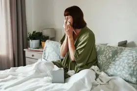 Donna a letto con fazzoletto, soffre di un raffreddore che non passa. Fazzoletti usati sparsi sul letto.