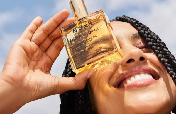 Una mano tiene una bottiglietta di Nuxe Huile Prodigieuse, un olio multiuso per viso, corpo e capelli. Scopri a cosa serve questo prezioso olio.