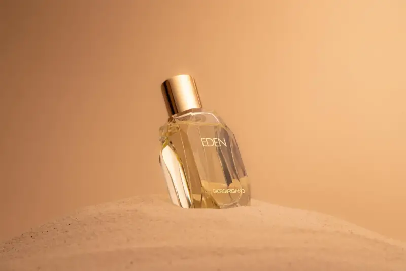 Flacone di profumo "Eden" su sabbia dorata. Un body mist cos'è? Una fragranza leggera per rinfrescarsi.